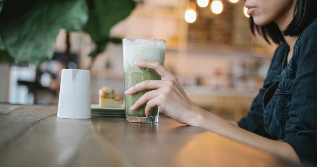 Pahar inalt de matcha latte cu gheata, tinut in mana intr-o cafenea