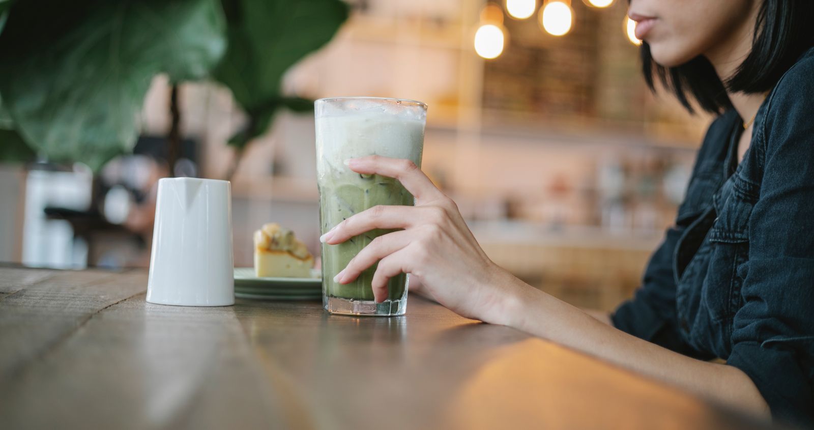 Pahar inalt de matcha latte cu gheata, tinut in mana intr-o cafenea